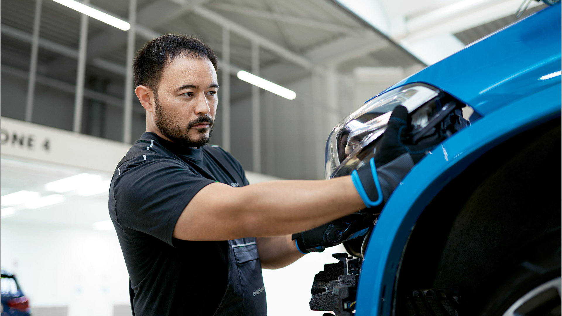 Homem a montar um farol num BMW azul num corredor de produção