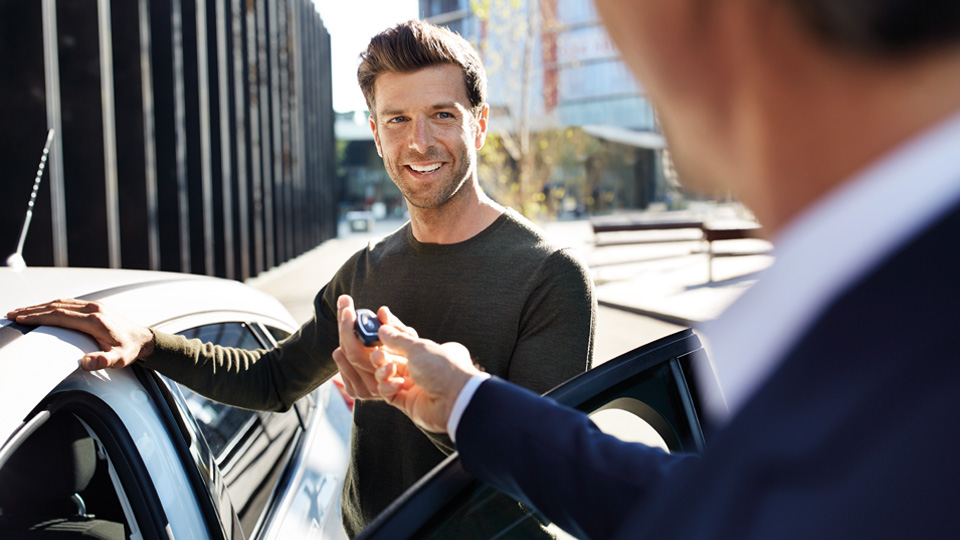 Man hands over the vehicle key to the BMW customer advisor Man stands at the open driver's door and hands over the vehicle key to the BMW customer advisor