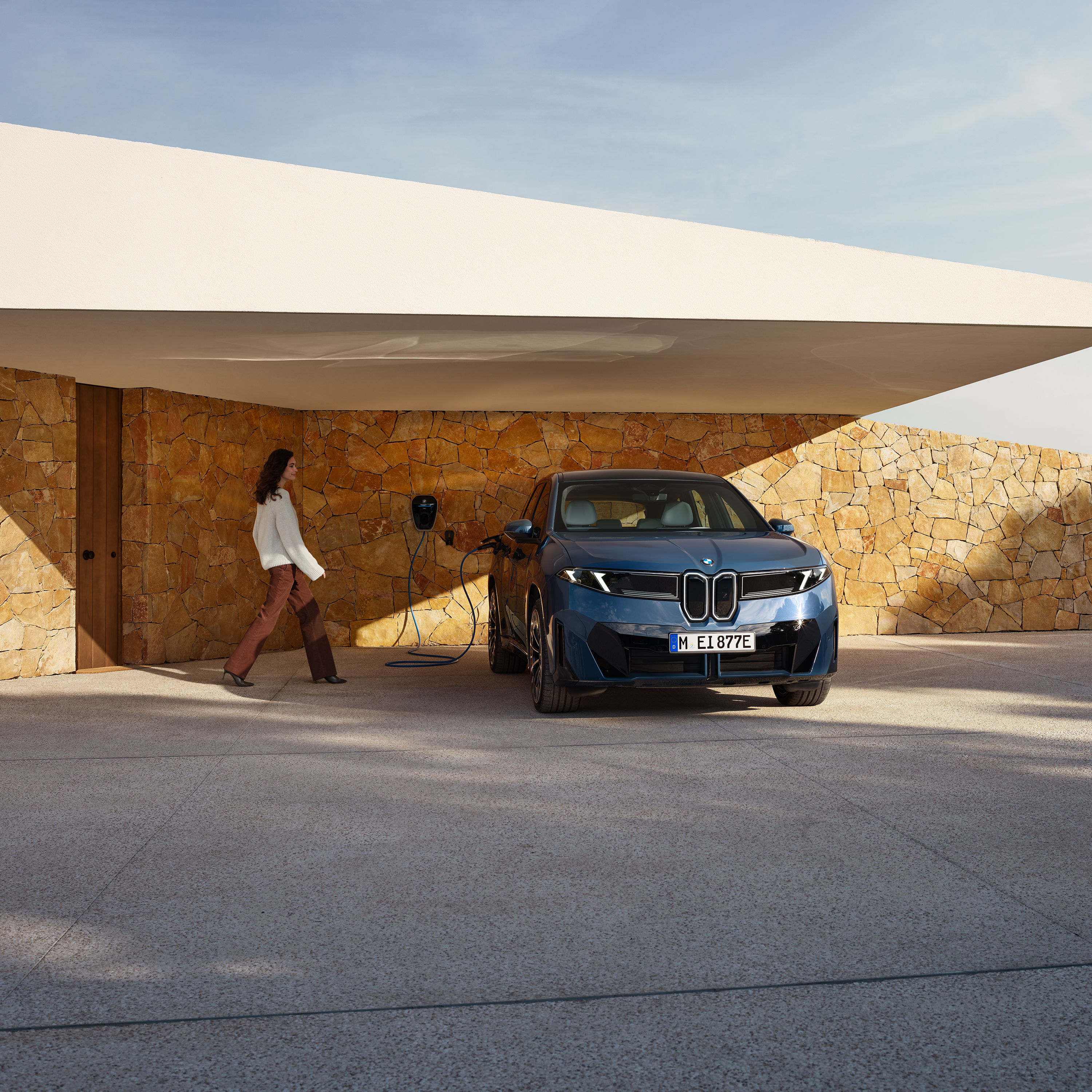 Uma mulher caminha em direção a um BMW iX3 ligado a uma wallbox